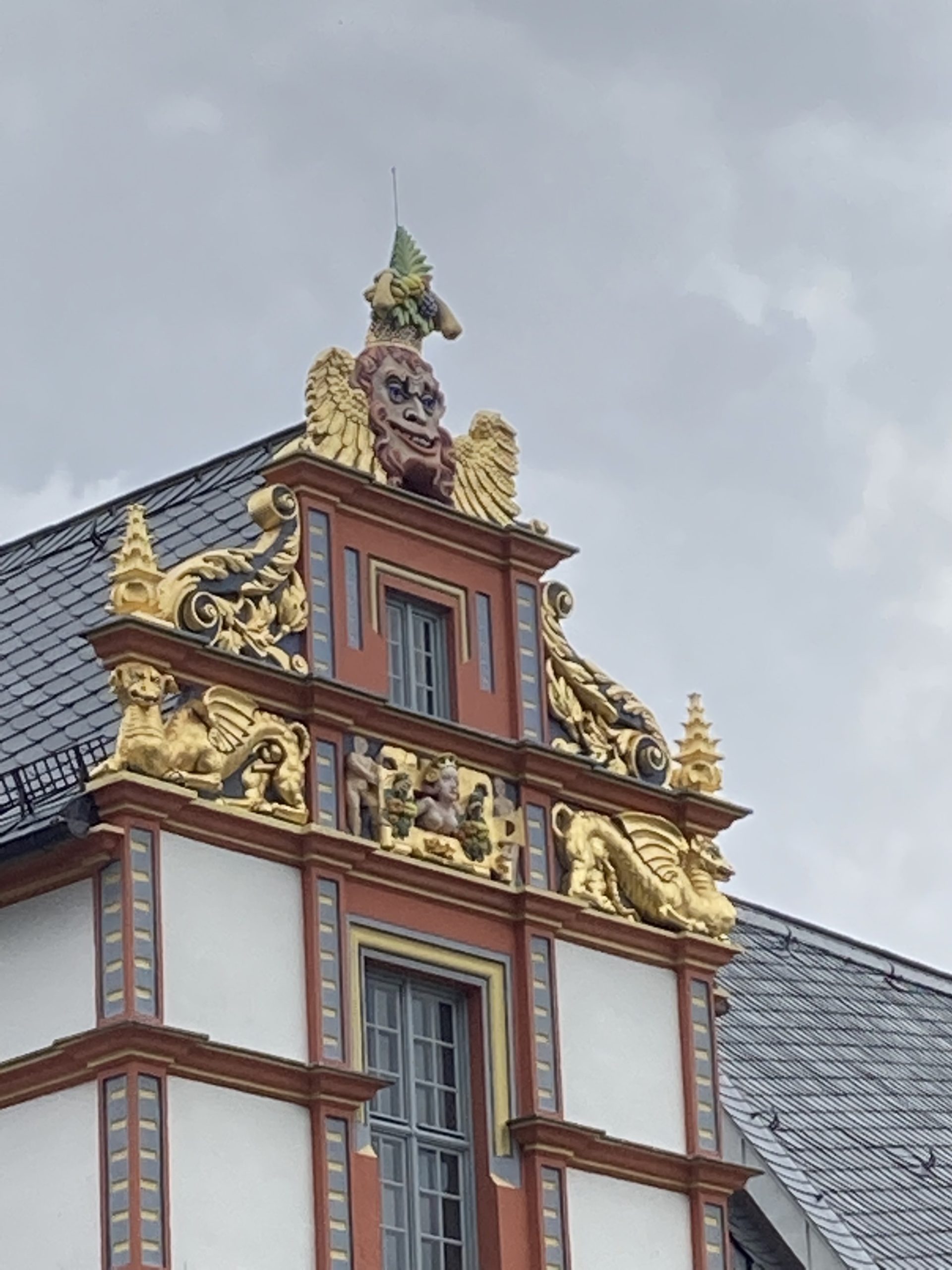 detail of an ornamented rooftop with gold-plated animals , a fertility goddesss and a strange leering face in bright colours