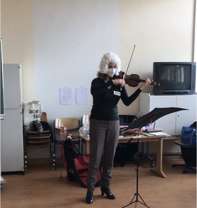 Fiona with a Bach wig on playing the violin in a classroom