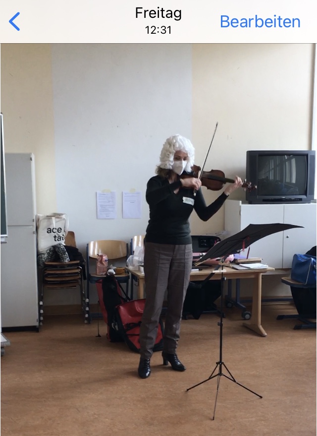 Fiona with a Bach wig on playing the violin in a classroom